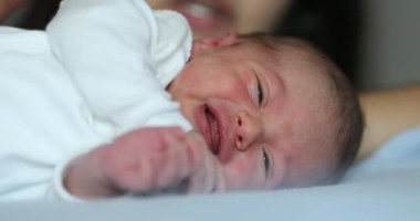 Newborn baby infant crying laying in bed, close-up of baby face crying