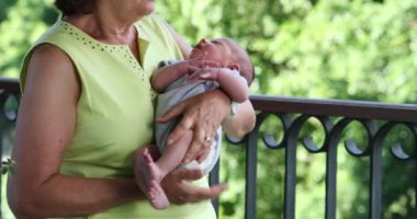 Candid grand-mother holding newborn baby infant in her arms outside