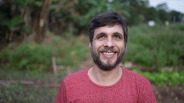 Portrait of a young man walking forward toward camera. Person walks in green agriculture farmland smiling