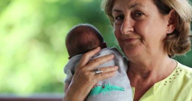 Portrait of grand mother holding newborn baby grand-son looking to camera