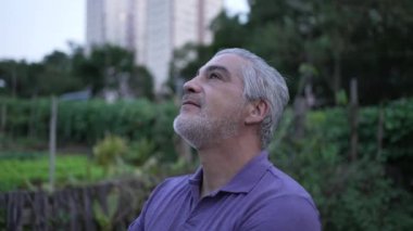 Meditative older man standing outside at park looking at sky in contemplation
