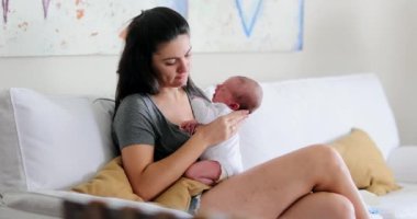 Candid mother holding newborn baby infant seated at home sofa