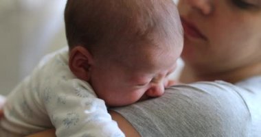 Mother holding newborn baby tapping at tired infant back