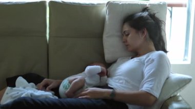 Authentic candid real life tired new mother with newborn baby at home trying to sleep and rest