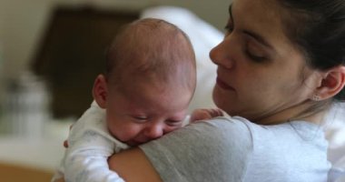 Mother holding newborn baby seated at home sofa