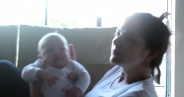 Candid mother holding newborn baby son at home casually on sofa