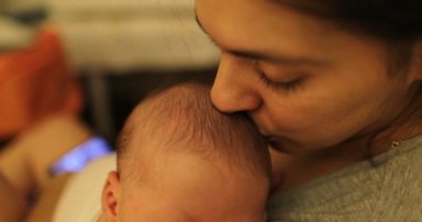 Mother kissing sleeping newborn baby face closeup