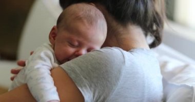 Mother holding newborn baby tapping at tired infant back