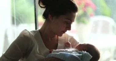 Candid mother holding newborn baby infant in her arms at home