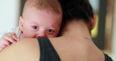 Newborn baby looking to camera while being held by mother