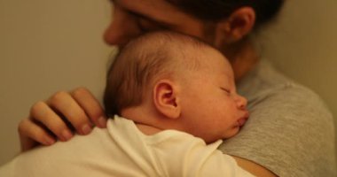 Candid mother holding sleeping newborn baby in the evening in bed