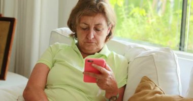 Senior older woman holding smartphone seated at home
