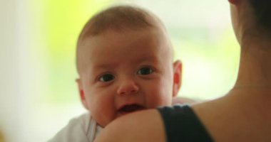 Baby newborn crying while being held by mother looking to camera