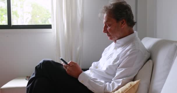 Older Man Seated Home Sofa Looking Smartphone Device — Vídeo de stock
