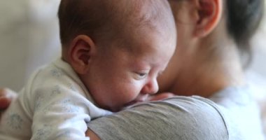 Mother holding newborn baby tapping at tired infant back