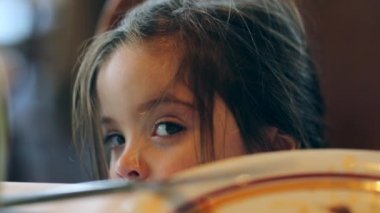 Little girl hiding behind table with mouth full adorable child grimace