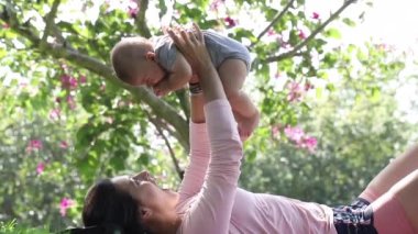 Mother playing with baby son outside in the park in nature raising toddler in the air