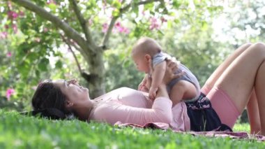 Mother playing with baby son outside in the park in nature raising toddler in the air