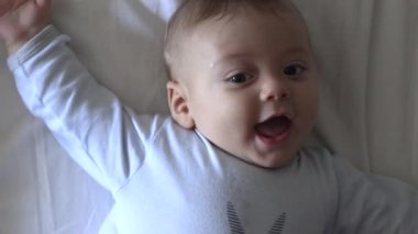 Baby infant layed in bed looking up to camera feeling happy