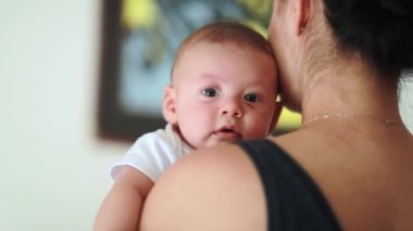 Baby looking at camera while being held by mom starring to viewer