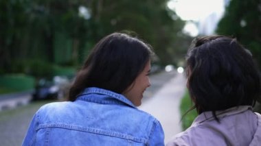 Back two young women walking outside together. Two female friends chatting