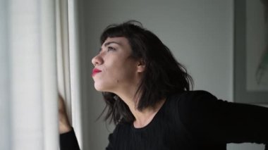 One beautiful hispanic girl looking out through curtain window checking sunlight day