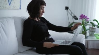 One hispanic latin girl opening computer laptop sitting at couch at elegant living room home