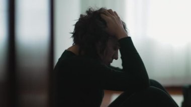 Depressed woman sitting on floor covering face with hands in despair
