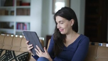 Happy woman browsing internet holding tablet at home living room. Person using modenr digital device smiling at media content