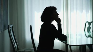 Anxious woman sitting at home in silhouette. Thoughtful person in contemplation feeling preoccupied
