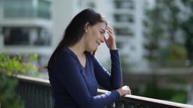 Happy woman standing home balcony thinking enjoying daylight. Pensive girl stand at apartment terrace