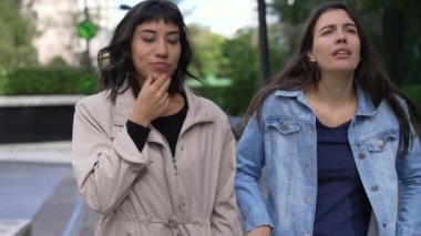 Two girlfriends walking outside gossiping together. Female friends in conversation on a walk