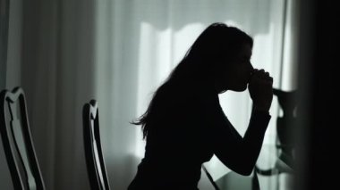 Silhouette of one depressed young woman sitting at home in the dark. Lonely girl suffering alone from mental illness