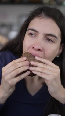 Woman eating tasty burger portrait face. Person takes a bite of hamburguer food. Vertical video