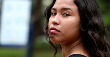 Confident mixed race hispanic woman standing outside looking at camera, casual real people series