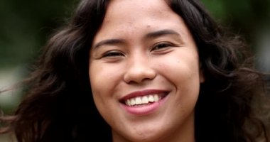 Happy hispanic woman standing outside at park smiling at camera. Mixed race latina girl portrait face, casual real people series
