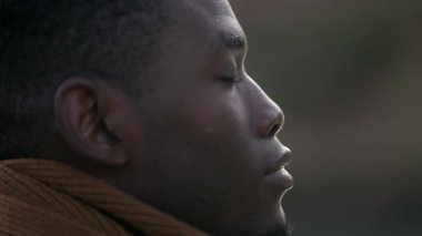 Black man taking a deep breath outside and opening eyes looking up at sky smiling feeling free