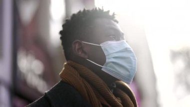 Black African man wearing covid-19 face mask standing outside in street looking at camera