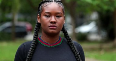 Confident black African young woman standing outside at park looking at camera