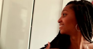 Genç Afrikalı kız aynanın önünde kendini kontrol ediyor. Aynadaki yansımanın önünde duran siyahi genç kadın.