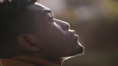 Hopeful African man looking up at sky, black person closing eyes in meditation and contemplation