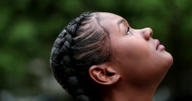 Thoughtful African woman in 20s standing looking at sky with HOPE and FAITH