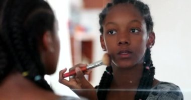 Mixed race girl applying makeup in front of mirror