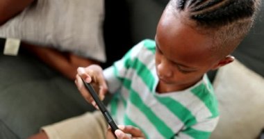 African siblings using cellphone at home. Black ethnicity children watching video on cellphone