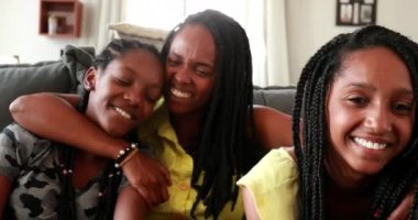 Mother hugging teen daughters. African mom embracing girls together at home sofa