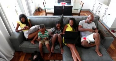African family sitting in couch looking technology gadgets