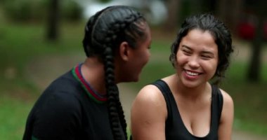 Two diverse friends laughing and smiling together. Mixed race girlfriends talking in conversation outside. Authentic real life laugh and smile