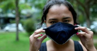 Hispanic woman putting covid-19 face mask outside looking at camera