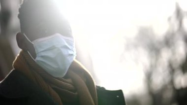African man standing wearing covid-19 face mask looking at camera with sunlight flare