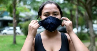 Young hispanic woman putting covid-19 face mask